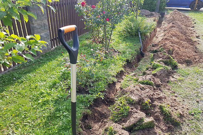 Backyard landscape being prepared for in ground wired lighting by digging a trench with two spear head shovels 