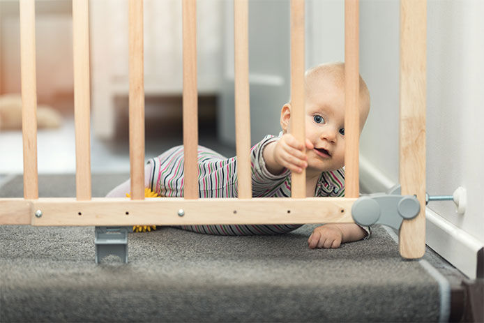 Baby at the top of the stairs on the ground holding on to the baby gate