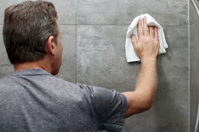 A man wiping a tile wall with a wash cloth