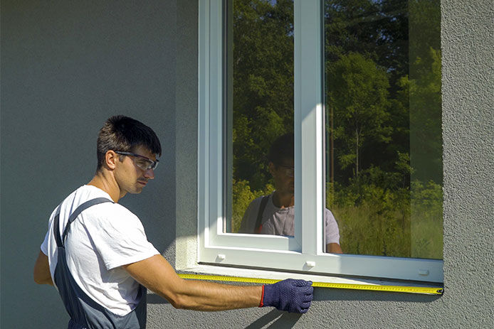 Man using a tape measure to measure the outside of a window