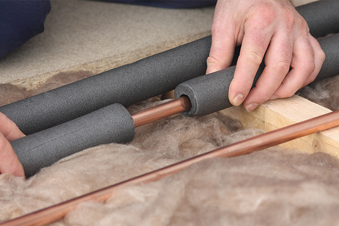 A man adding foam insulation to copper pipes to help keep the pipes from freezing in the winter time 