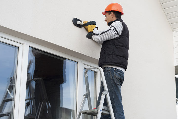 Man standing on a ladder to mount the back of an outdoor security light