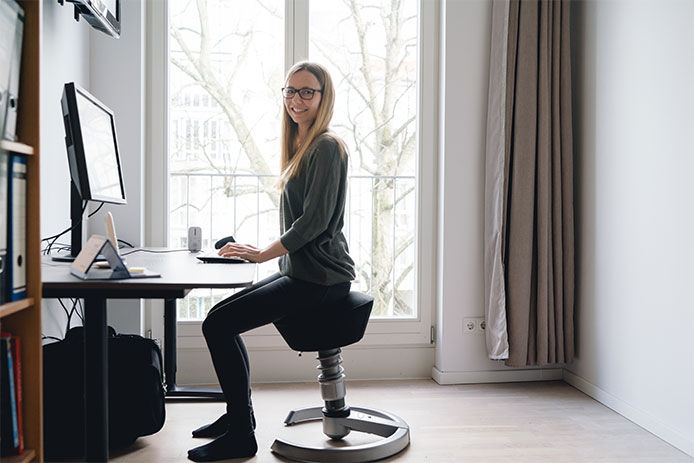 Woman sitting on desk chair and smiling as she is on the computer