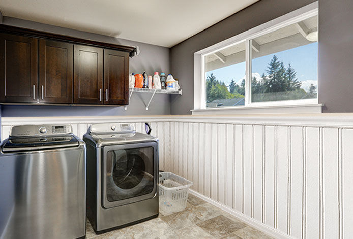 Grey laundry room with modern stainless steel washing machine and dryer, brown cabinets and tile floor.