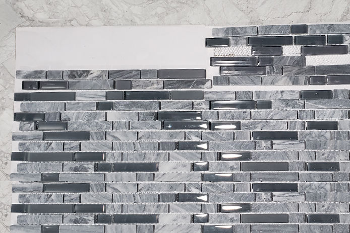a top down view of glass tile backsplash that is a variety of grays 