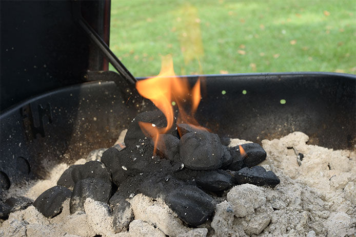 Using a lighter to light the charcoals with lighter fluid on them