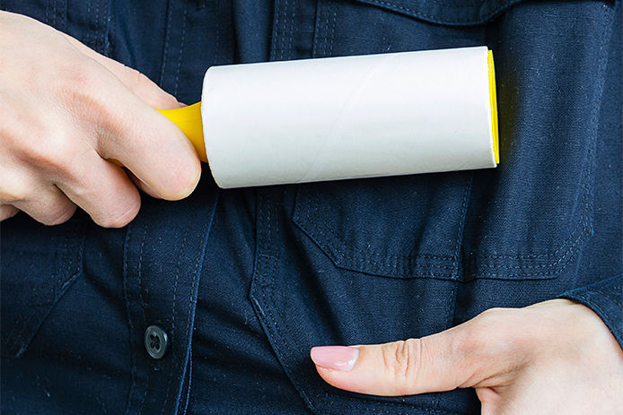 a lady wearing a dark blue jean shirt running a yellow lint roller over her clothing.