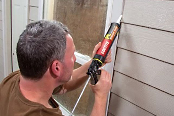 close up of a man caulking up an outside window using polyurethane caulk