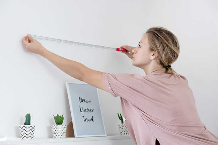 Woman measuring an empty space on a blank wall