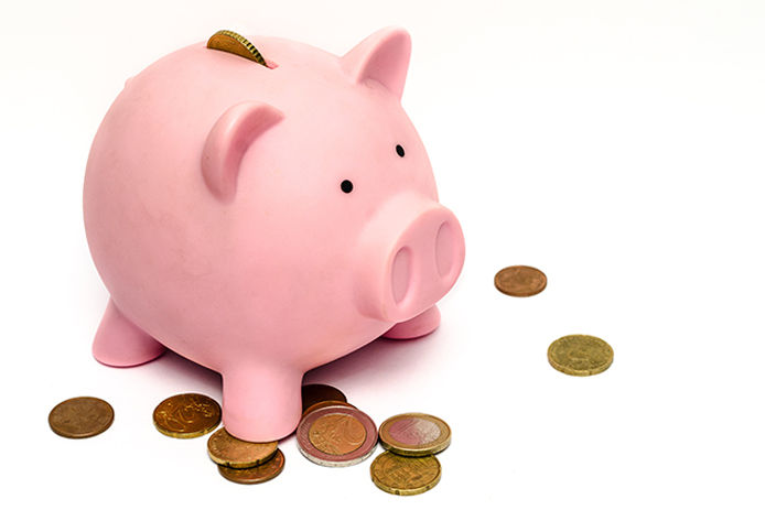 A pink piggy bank with coins under it and going into the top slot on a white isolated background