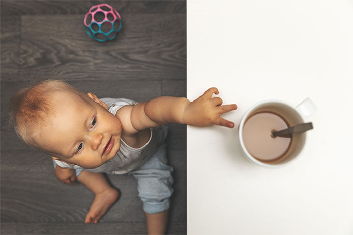 Baby reaching up a coffee table to touch a hot cup of coffee