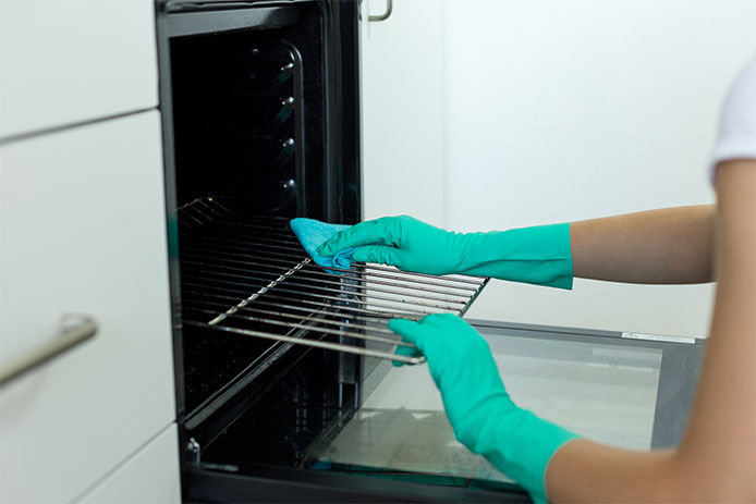 Person wearing teal rubber cleaning gloves cleaning the grate of the oven