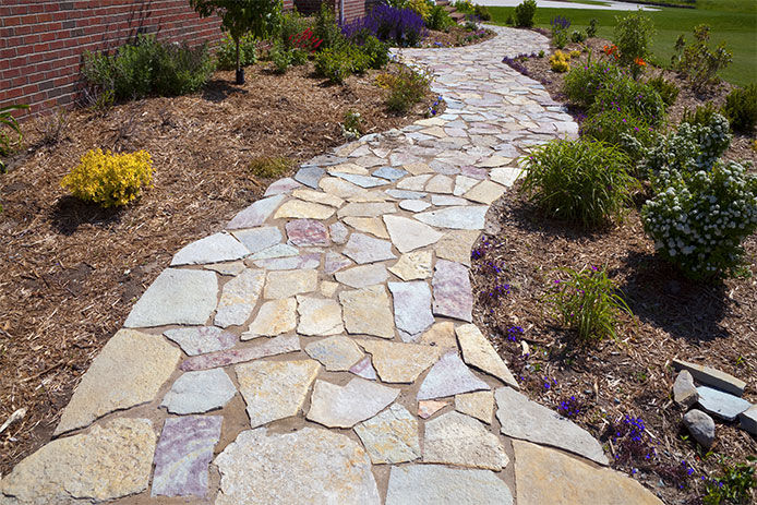 A stone tiled pathway surrounded with wood chipped mulch and landscaping