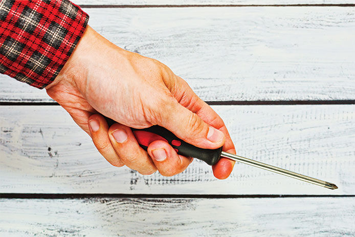 A person holding a screwdriver in their hand against a wood background