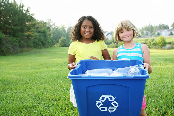 Two girls smiling holding a recycling bin with plastics in it