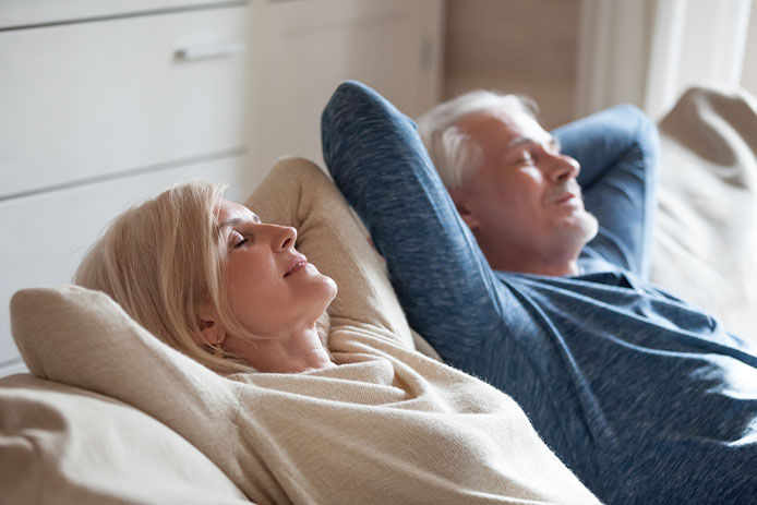 An elderly couple sitting on a couch with their arms behind their heads breathing in deep relaxing