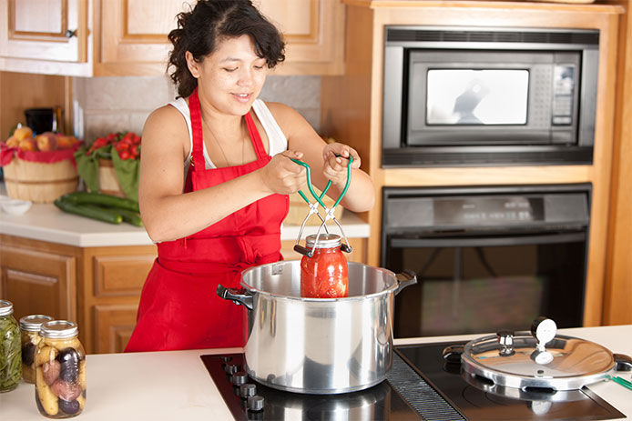 Woman pulling the canning jars out of pot of hot water with tongs