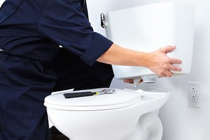 A professional installing the back end of a toilet tank