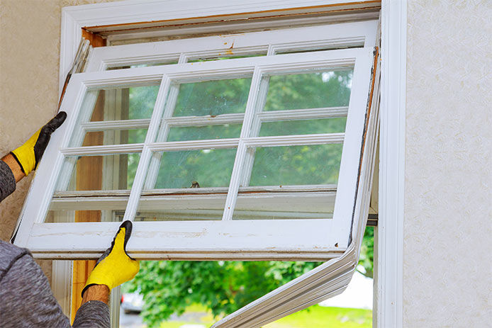 Person wearing work gloves pulling an old window out to replace