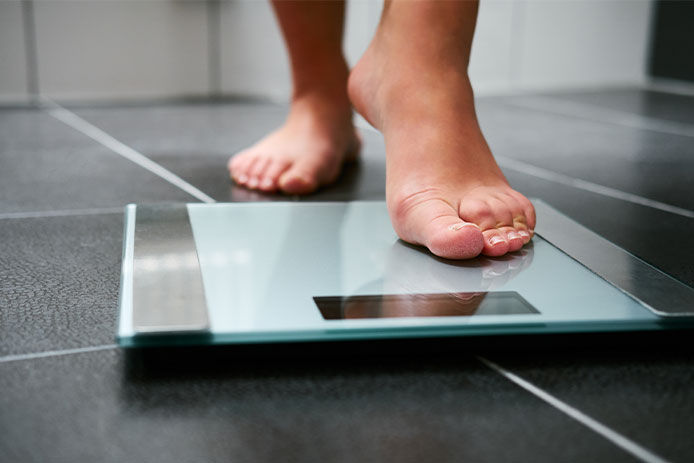 A person standing on a glass scale weighting themselves