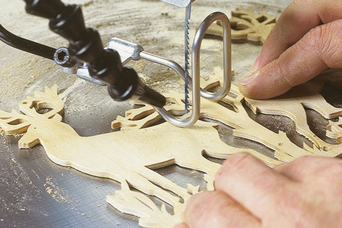 close up of a man using a scroll saw to cut out a decorative deer in wood