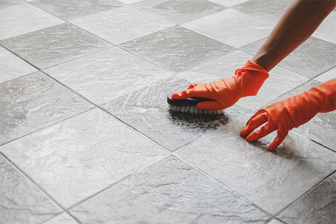 A person wearing orange gloves and scrubbing a tile floor