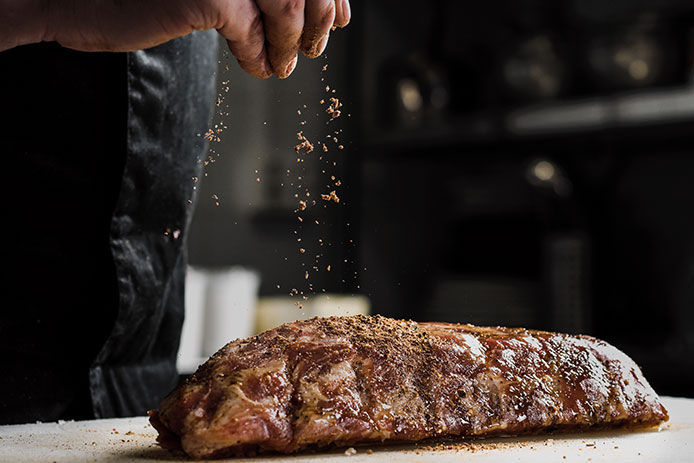 Man sprinkling seasoning on a slab of meat