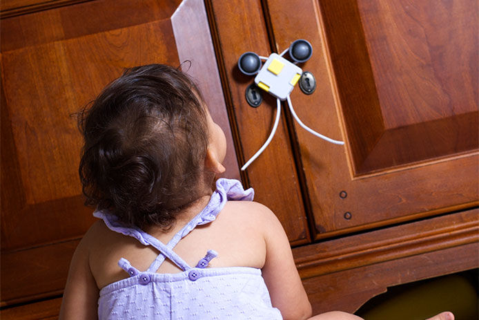 Baby looking at a child proof lock on a cabinet