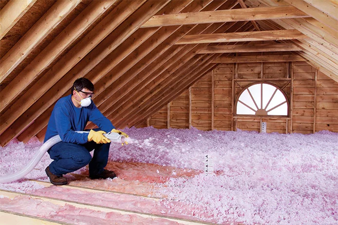 Man wearing PPE and spraying insulation in an attic