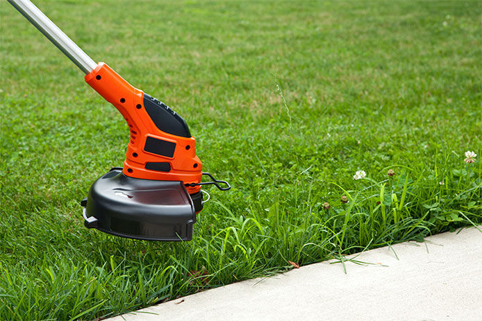 Weed wacking with a string trimmer next to sidewalk