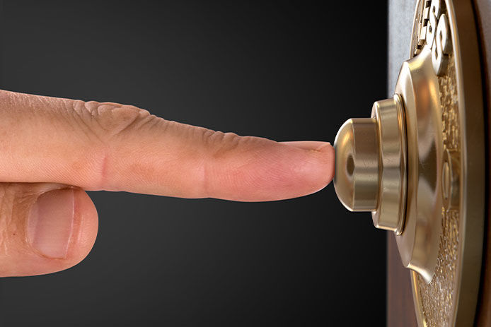 A close up of a finger pushing a gold doorbell sideview. 