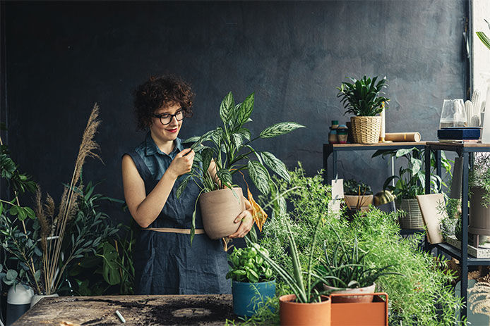 Woman holding a potted plant while surrounded by many different plants