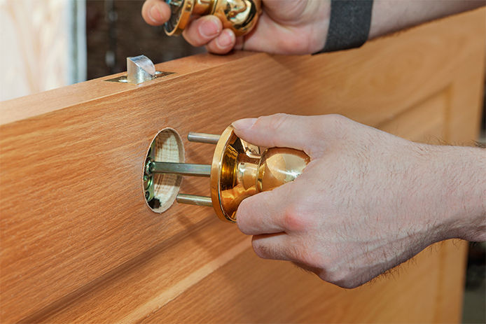 Taking the doorknob piece featuring a long metal spindle and threading it through the latch
