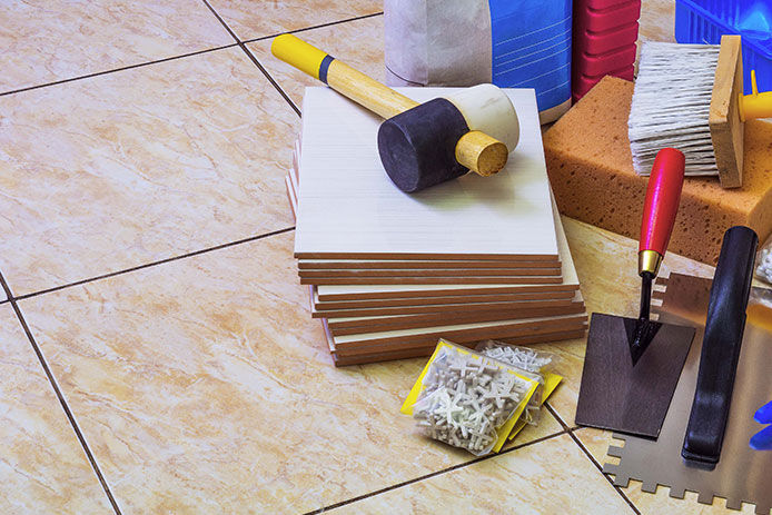 Stack of tile, tile spacers, rubber mallet, trowels all laying on ceramic tile flooring