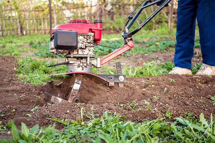 Person with a tiller working their garden soil