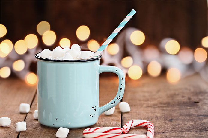 A traditional cup of hot chocolate filled with marshmallows and candy canes beside it