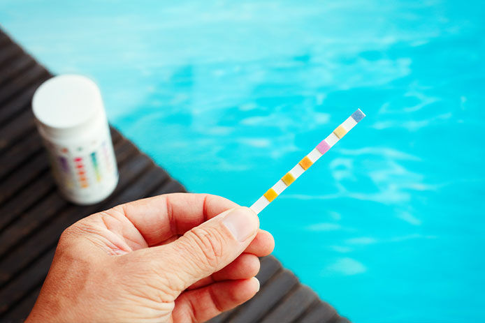 Person holding a pH testing strip with clear pool water in the background