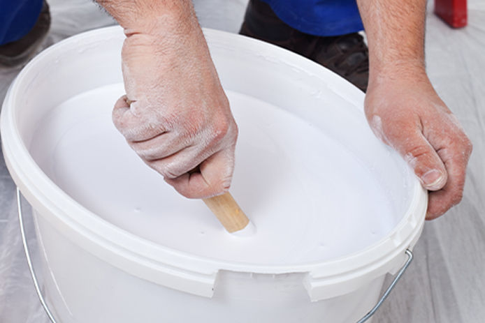 Man mixing paint in a 5 gallon white bucket 