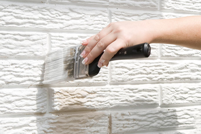 Woman using a 3" paint brush to apply white paint to a brick wall