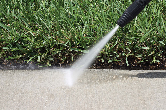 A close-up of a power washer cleaning the sidewalk