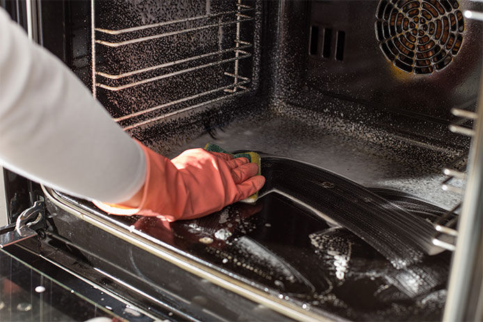 Person wearing pink rubber cleaning gloves cleaning the inside of their oven with a sponge