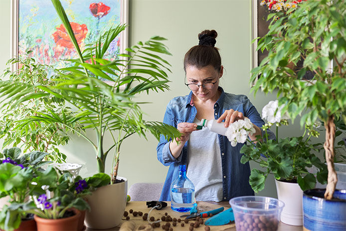 Woman surrounded by many potted plants on tabletop while she measures a liquid out