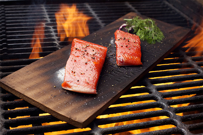 A type of fish cooking on a slab of wood on grill grates