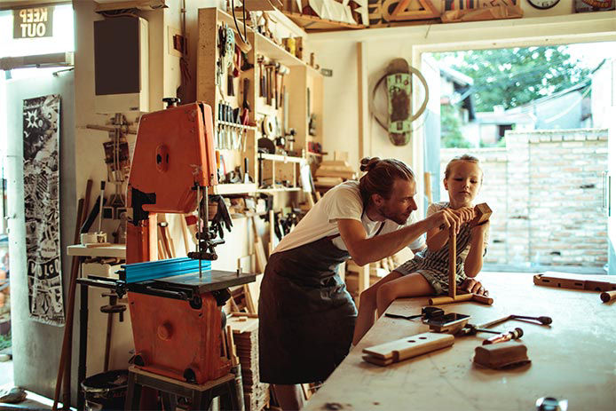 Man working in his garage woodworking shop with his daughter watching