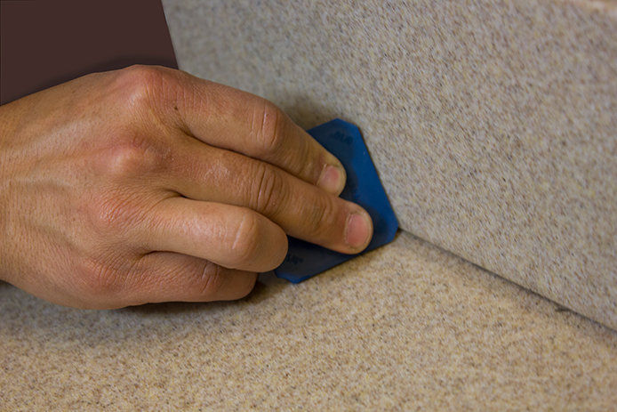 A close up image of a hand using a blue square caulking tool to smooth out caulk lines on a tiled surface