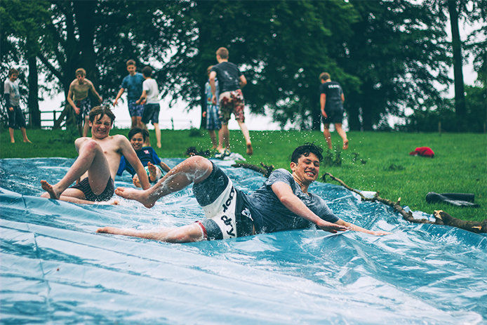 a group of teenage boys sliding down a tarp style slip and slide