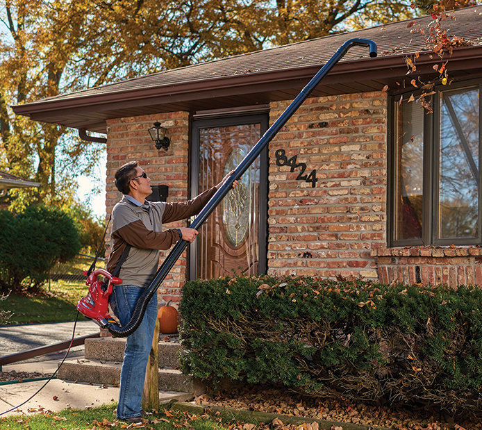Man using a leaf blower with extension to reach gutter to blow leaves out