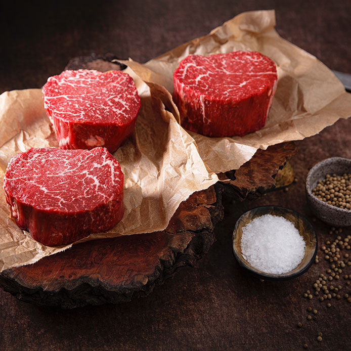 three 6 ounce filet mignon on butcher paper with salt and pepper in a small wooden bowl next to the steaks