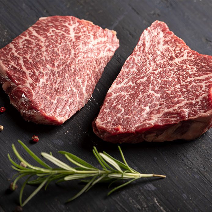 Two Japanese kobe beef steaks resting on a butcher block with a sprig of thyme in the foreground.