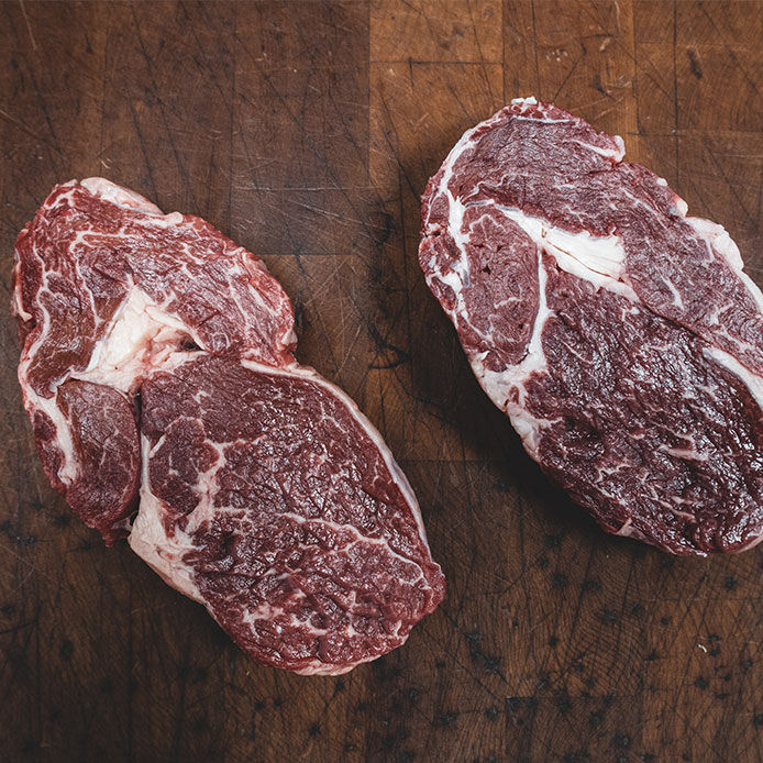 Two marbled ribeye steaks on a butcher block